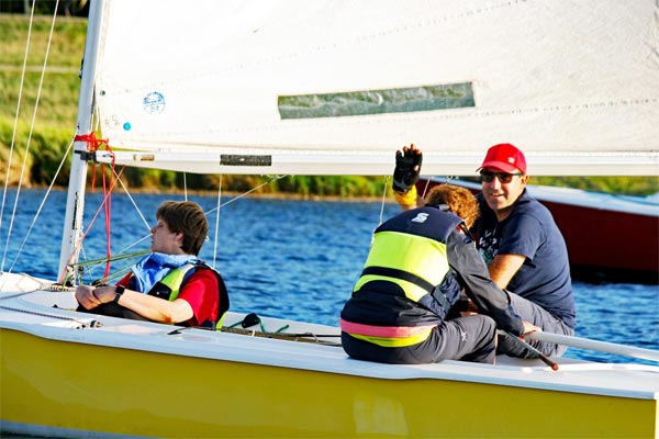 Auf dem gelben Kielboot mit weißem Segel sitzen zwei blinde Frauen und ein Skipper