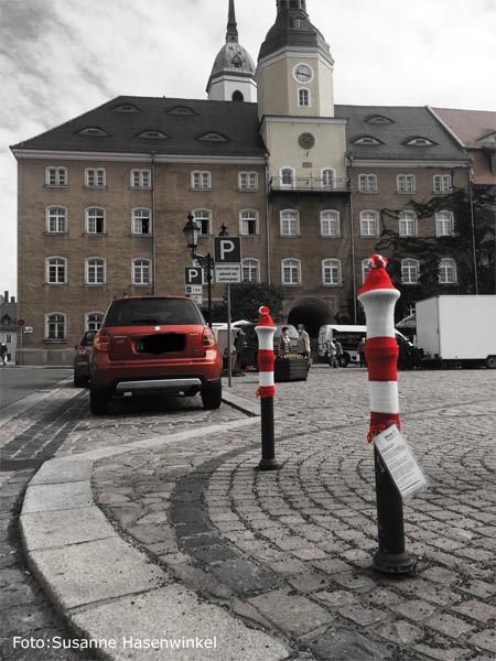 Marktplatz in Roßwein mit Rathaus, zwei graue Poller tragen rotweißgestreifte Mützen