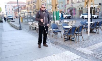 Mann mit Blindenstock orientiert sich an der Bushaltestelle