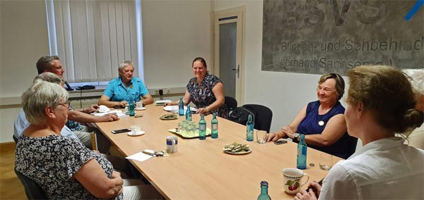 Um den Konferenztisch Blinden- und Sehbehindertenverband Sachsen e.V. sitzt an der hinteren Stirnseite Herr Schneider (stellvertretender Landesvorsitzende) links sitzen Herr Hauschild (Vorstand BSVS), Herr Freudenberg (Vorstand BSVS) und Frau Freudenberg (Begleitperson von Herren Freudenberg). Auf der rechten Tischseite haben Platzen genommen Frau Čagalj Sejdi (Bündnis 90/Die Grünen), Frau Börner (Fachgruppe Taubblinde), Herr Börner (Begleitperson Frau Börner) und an der vorderen Stirnseite Frau Meilert (Leiterin Landeshilfsmittelzentrum).