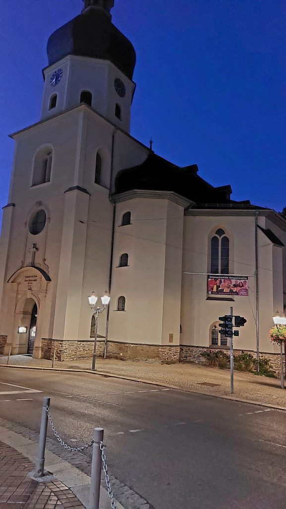 Auch zur Geschichte der 300 Jahre alten Lutherkirche erfuhren die Teilnehmer des Nachtwächterrundgangs zur Woche des Sehens viel Interessantes. Schräge Ansicht auf die Lutherkirche. Der Hintergrund ist ein dunkelblauer Nachthimmel. Vor der Kirche ist ein gepflasterter Gehweg mit zwei leuchtenden Laternen, einer Ampel und zwei Pollern. Danach folgt die Straße und am unteren linken Bildrand ist wieder ein Stück gepflasterter Gehweg.