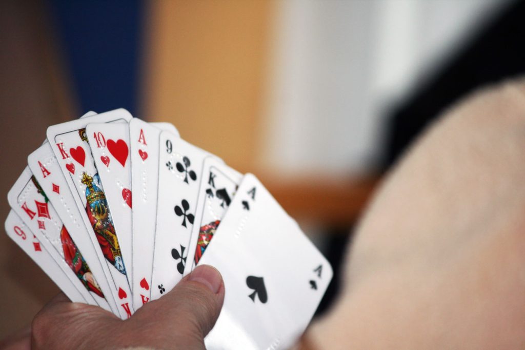 Eine Person hält ihre Spielkarten in der Hand, welche mit Punktschrift adaptiert wurden. Der Hintergrund ist verschwommen.