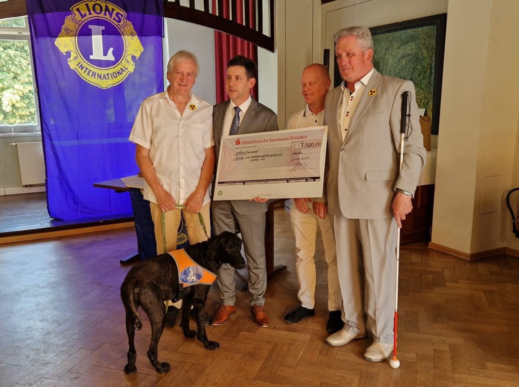 Auf dem Bild von links nach rechts stehen Herr Schneider (Landesvorsitzender BSVS, Herr Kästner (Club-Präsident Lions Club Dresden Centrum), Herr Adam (Finanzbuchhalter BSVS) und Herr Hauschild (erster stellvert. Vorsitzender BSVS) und halten den Spendencheck gemeinsam in der Hand. Im Vordergrund steht der Blindenführhund von Herrn Schneider.